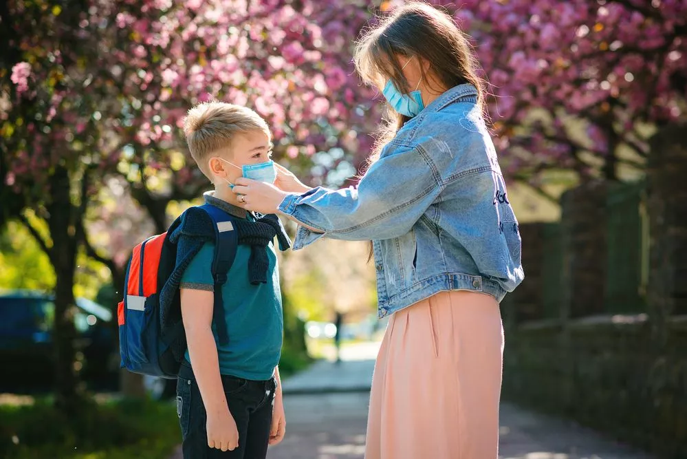 A woman helping her son get ready for school by wearing a surgical face mask