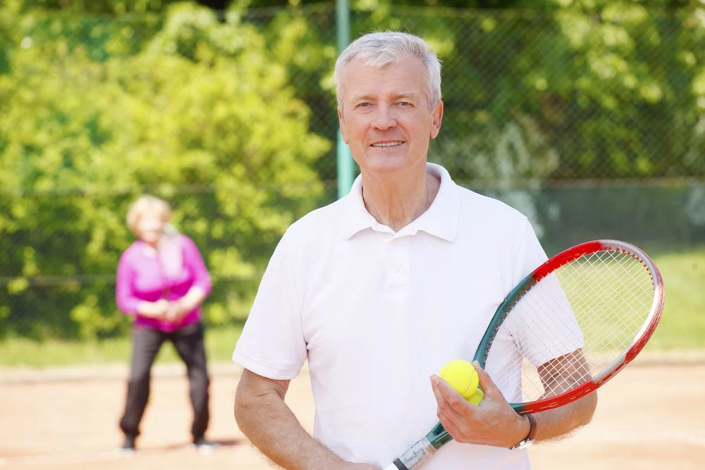 A senior man with a tennis racket on a court.