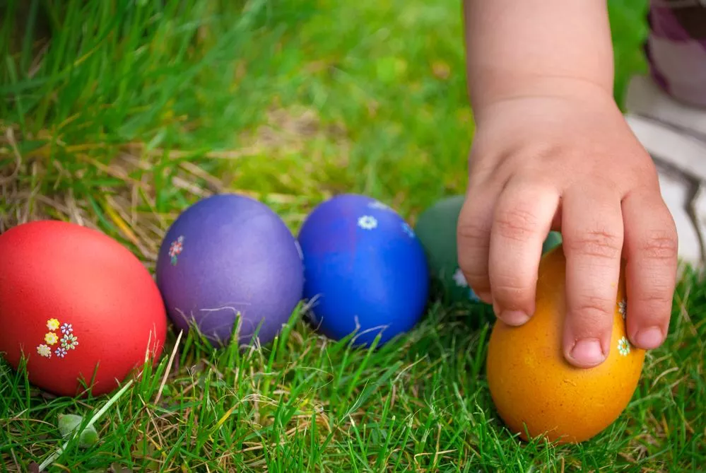 A toddler's hand is picking up one of a cluster of colorful Easter eggs