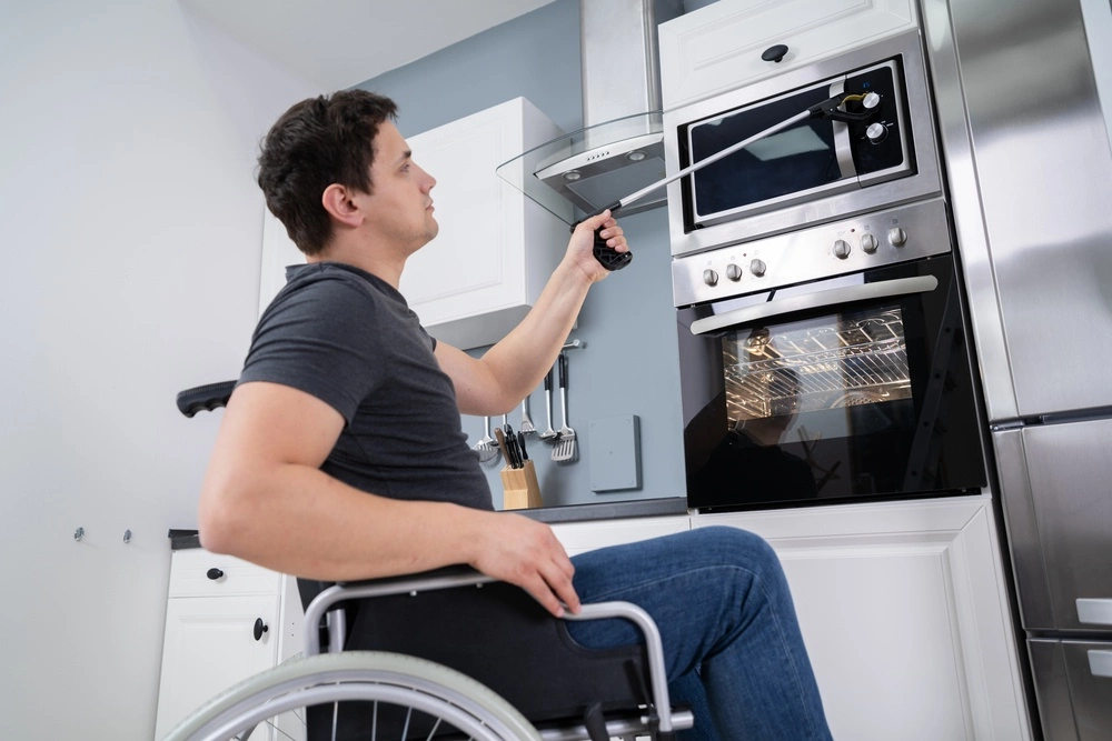 A man in a wheelchair is using a reacher in the kitchen.