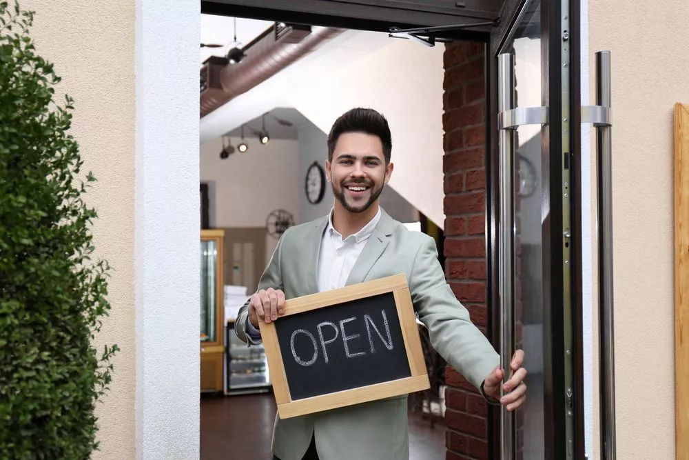 A business owner is holding an open sign in the doorway.