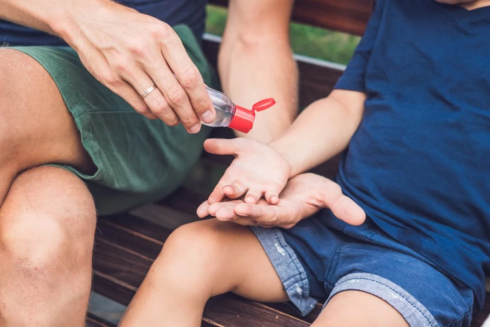 A parent giving a child hand sanitizer on a bench.