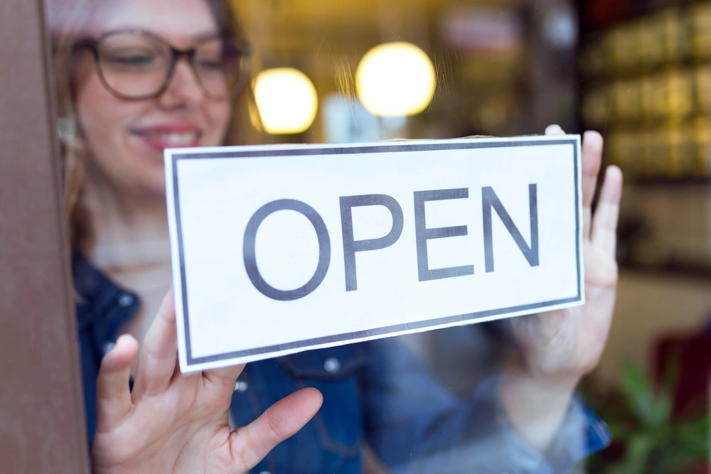 A woman opening up her store with an open sign in the window