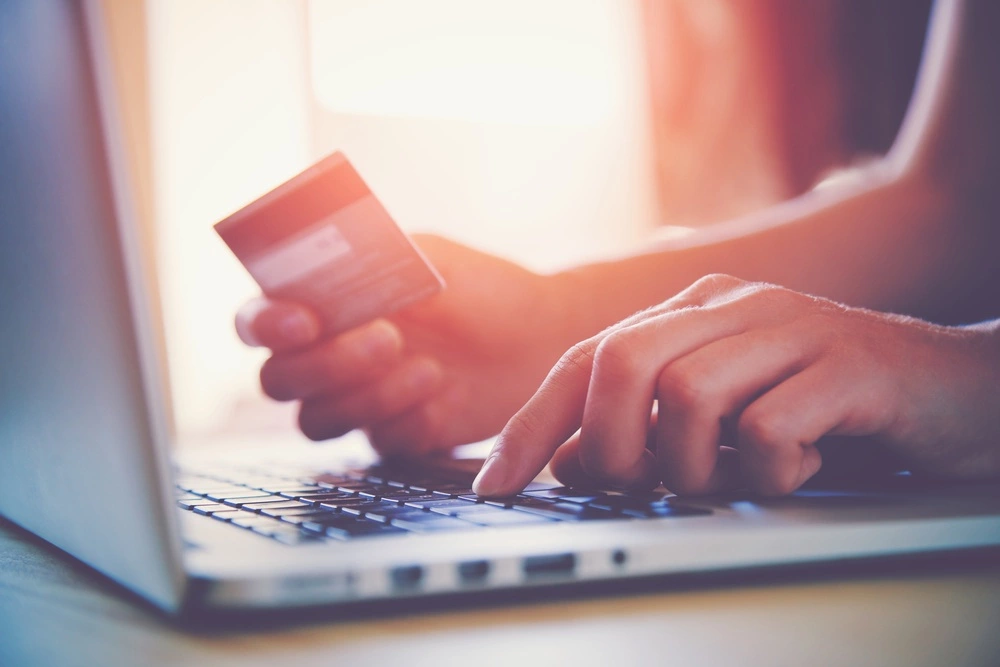 A person's hands are shown with a credit card while typing on a laptop.